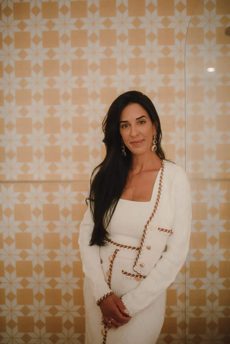 Ive Bitencourt standing in a white outfit in front of a patterned tile wall